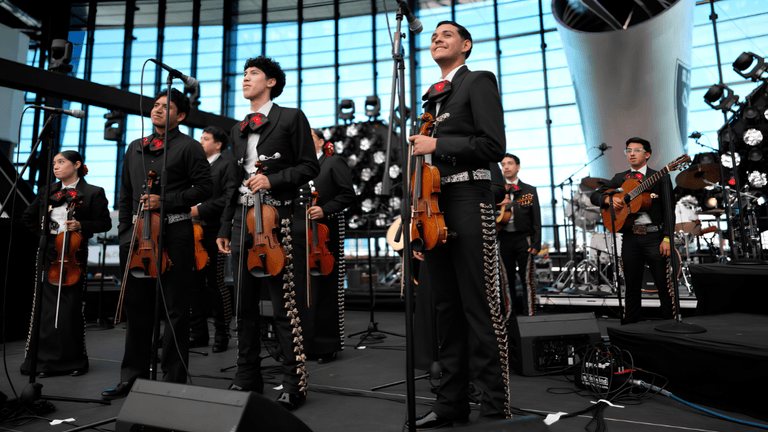 A mariachi band performs on stage with instruments and traditional attire in a modern venue